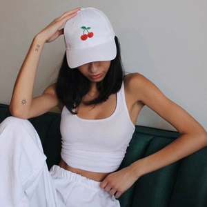 Detail of white cotton baseball cap with red cherry embroidery worn by a model