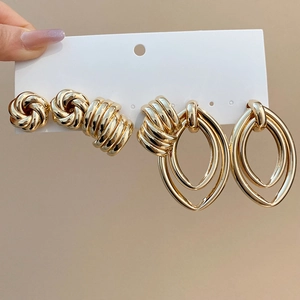 Close-up of golden metal knot stud earrings and twisted oval geometric drop earrings