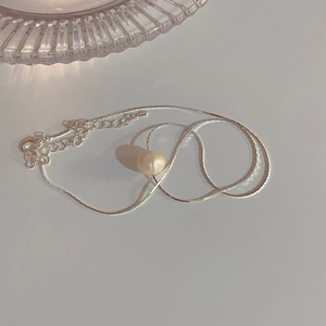 Macro detail of a silver snake chain necklace featuring a single round white pearl