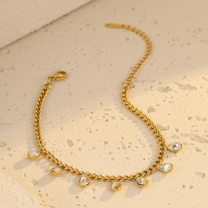 Detail of gold chain bracelet featuring water drop crystal charms on a beige stone surface