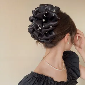 Dettaglio di un grande fermaglio per capelli in raso nero con perle bianche sul retro