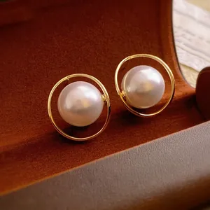 Elegant gold-plated hoop earrings with a large white pearl center on brown velvet