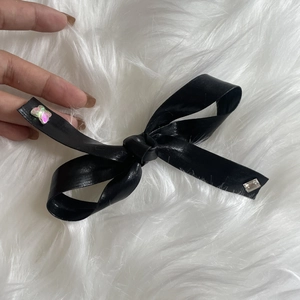 Close-up of black leather bow hair clip with sparkling gems on a soft plush background
