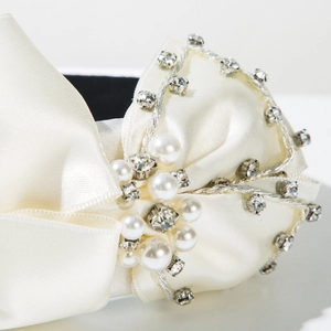 Gros plan du serre-tête en satin avec perles blanches, strass et détails de nœud chic