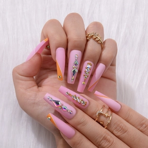 Detail of matte pink long coffin press-on nails with rhinestones and orange stripe accents