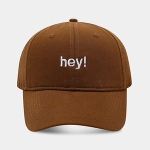 Detail of white hey embroidery on tan cotton baseball cap with high texture finish