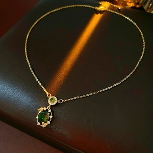 Close-up of luxury gold-plated necklace featuring emerald green gemstones and crystal detail
