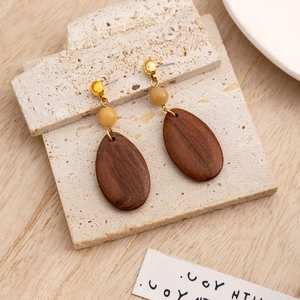 Macro view of geometric wooden drop earrings with natural wood grain and cream bead