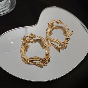 Macro shot of gold irregular geometric hoop earrings on a black reflective background