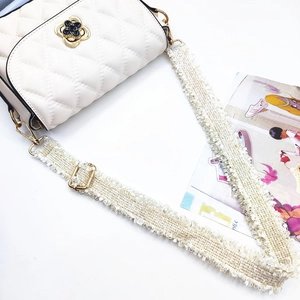 Close-up of adjustable woven tassel shoulder strap with gold metal buckle on cream crossbody bag
