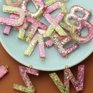 Pink and yellow glitter resin alphabet letter charms with gold loops for DIY jewelry making.