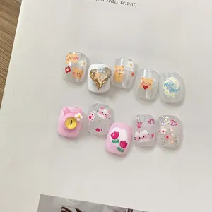 Detailed view of handmade press-on nails with cartoon bear, heart rhinestones, and tulips