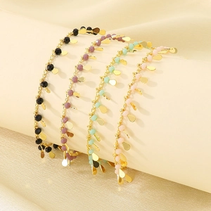 Detail of four colorful drip oil fishtail anklets with golden charms on a beige cylinder
