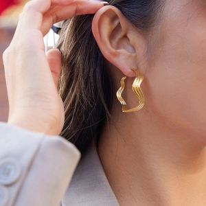 Close-up of golden wave C-shaped earrings on a model showing modern minimalist style