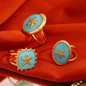 Macro shot of gold-plated starfish rings with light blue enamel on red velvet