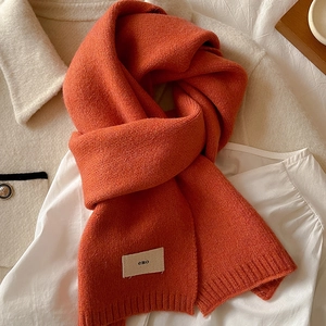 Close-up of soft orange knitted scarf with emo tag on white shirt and beige coat