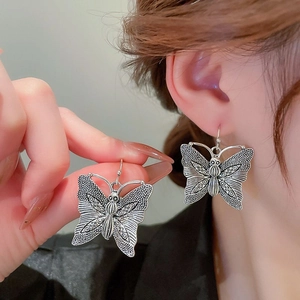 Detail showing vintage silver butterfly drop earrings with engraved texture on a model