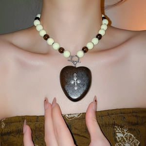 Détail du pendentif cœur en bois avec croix argentée sur un collier ethnique