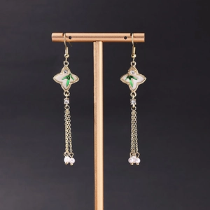 Detailed shot of long gold tassel earrings with white flower and green enamel bamboo leaf