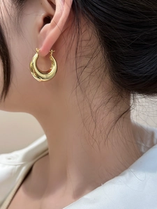 Close-up of a woman wearing chunky gold hoop earrings with a polished metallic finish
