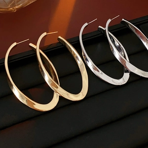 Macro detail of twisted oval metal hoop earrings in gold and silver finish