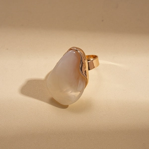 Détail d'une bague dorée ornée d'une grande pierre en résine crème en forme de goutte d'eau