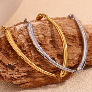 Detail of gold and silver bamboo tube bracelets on a textured wooden block and beige fabric