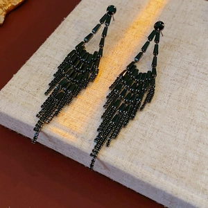 Macro detail of black crystal droplet tassel earrings on a textured fabric surface