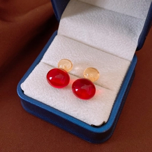 Détail des boucles d'oreilles boules en acrylique ambre et rouge foncé dans un écrin bleu