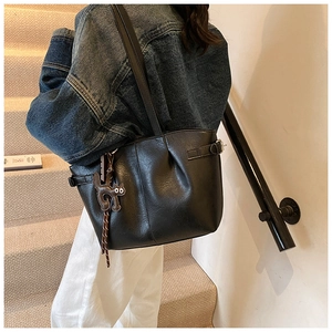 Detail of black pleated leather tote bag with a cute cat charm shown on model's shoulder