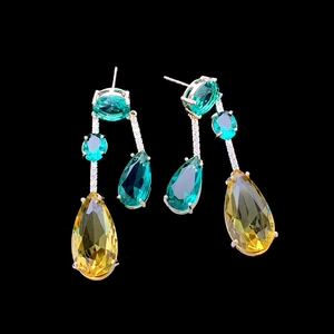 Detailed view of yellow and green teardrop earrings with luxury metal inlay on black background