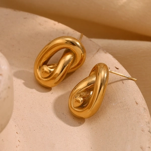 Macro shot of 18K gold plated knotted heart stud earrings on a textured stone surface