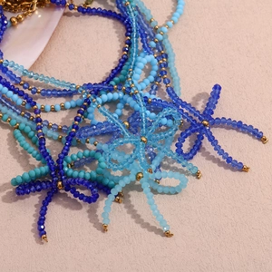 Handmade necklace with blue faceted crystal beads and gold accents on pink background