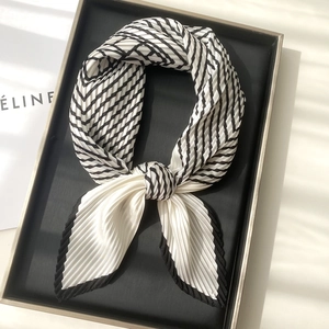 Elegant black and white striped pleated scarf displayed in a luxury gold rimmed tray