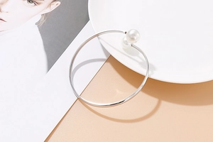 Detail of minimalist silver open bracelet featuring double pearls on elegant magazine decor