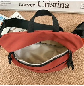 Detail of brick red waterproof nylon crossbody bag with interior lining and dual zippers