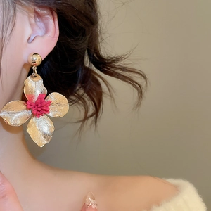Macro view of gold flower earrings with red textured centers worn by a model