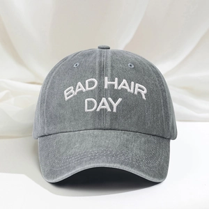 Detailed close-up of white BAD HAIR DAY embroidery on grey washed denim baseball cap