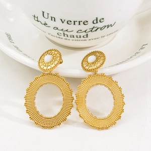 Detail of bohemian gold earrings with sunburst shell inlay and hollow mesh rings on ceramic