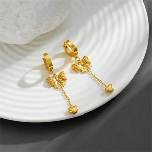 Elegant gold bow and heart pendant earrings displayed on a white textured plate