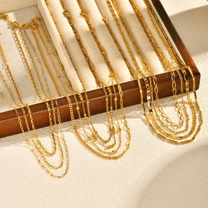 Various gold layered necklaces with beaded and twisted chain links on a wooden display stand