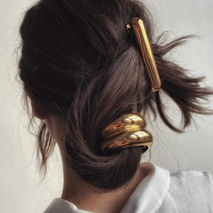 Close-up of polished gold metal hair cuff and barrette on a ponytail in minimalist style