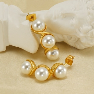 Detail of gold pearl earrings with three pearls in S-curve design on white statue base