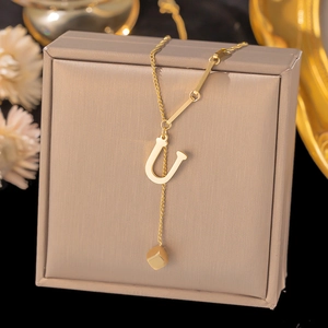 Close-up of golden necklace with letter U pendant and cube charm on a jewelry box