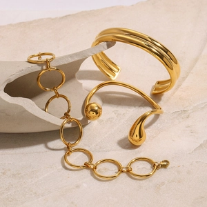 Modern gold-plated stainless steel bracelet set displayed on a textured stone base