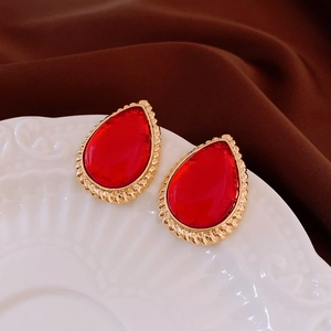 Detail of vintage red teardrop earrings with gold textured edges on a white ceramic plate