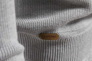 Macro view of grey ribbed knit sweater detailing a leather brand logo and stitching