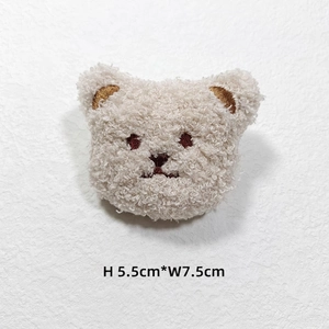 Close-up of cream plush bear accessory with embroidery, measuring 5.5cm by 7.5cm
