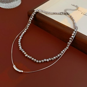 Detail shot of a double-layered necklace with silver irregular beads and metal tube pendant