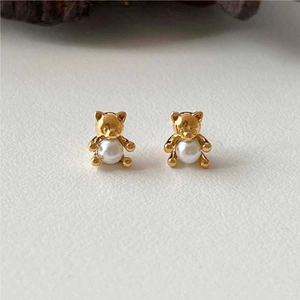 Macro detail of golden bear earrings featuring a white round pearl center on a beige base